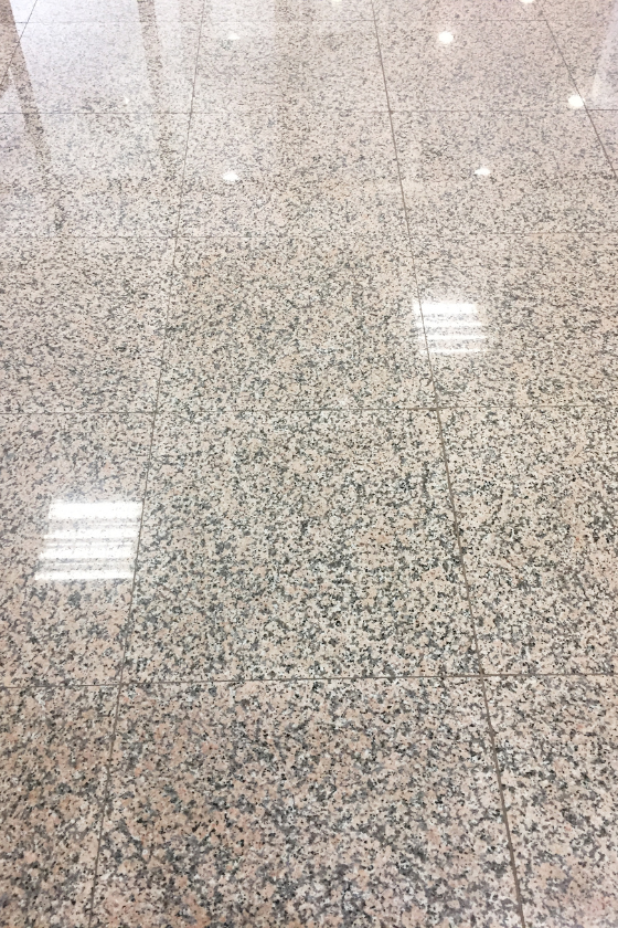 A close up of a shiny granite floor with reflections of lights.