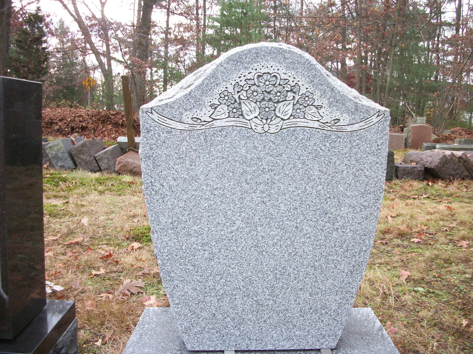A blank gray granite tombstone with a carved floral design at the top, standing in a cemetery.