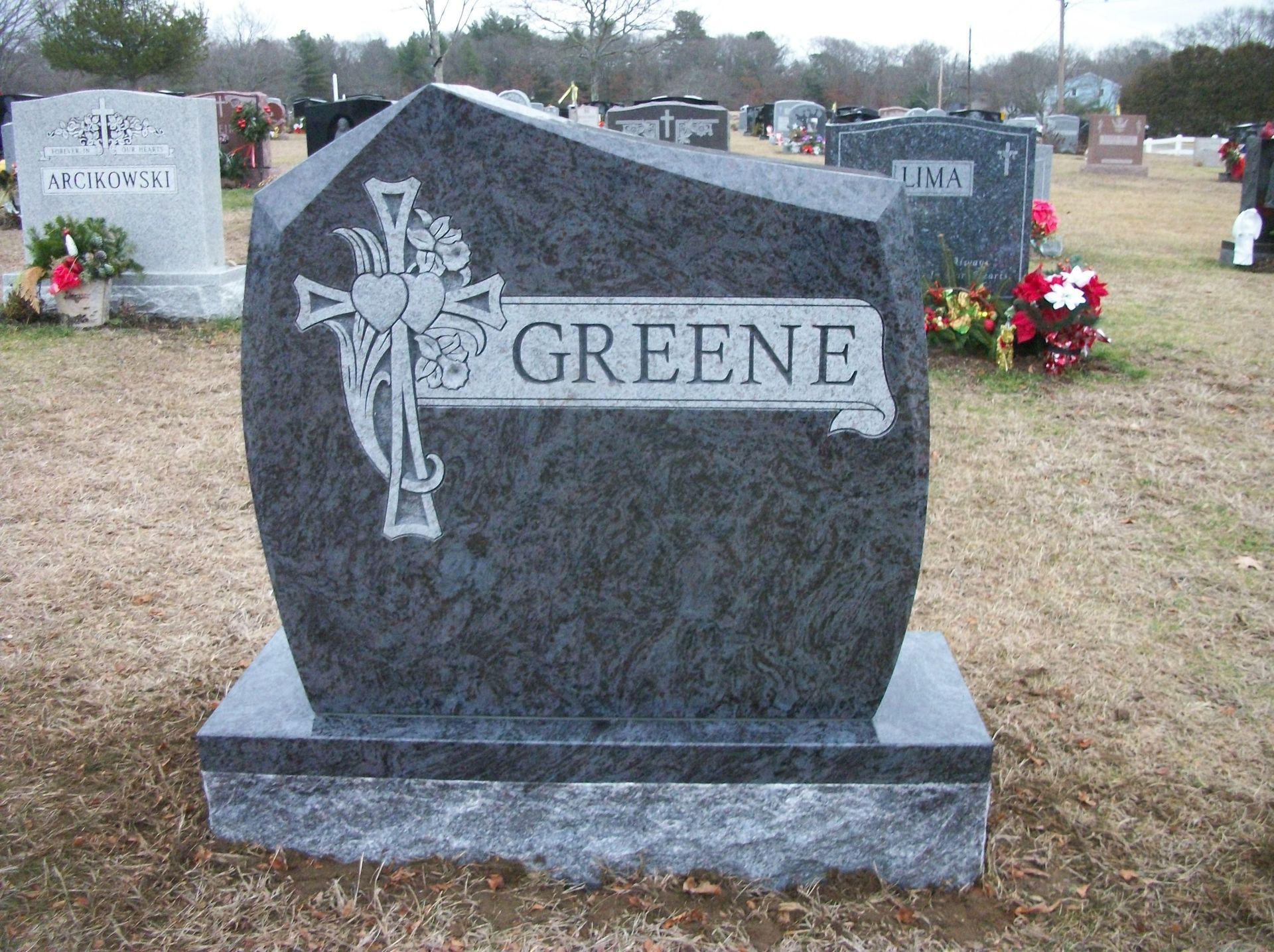 A dark granite gravestone engraved with a cross and the name 