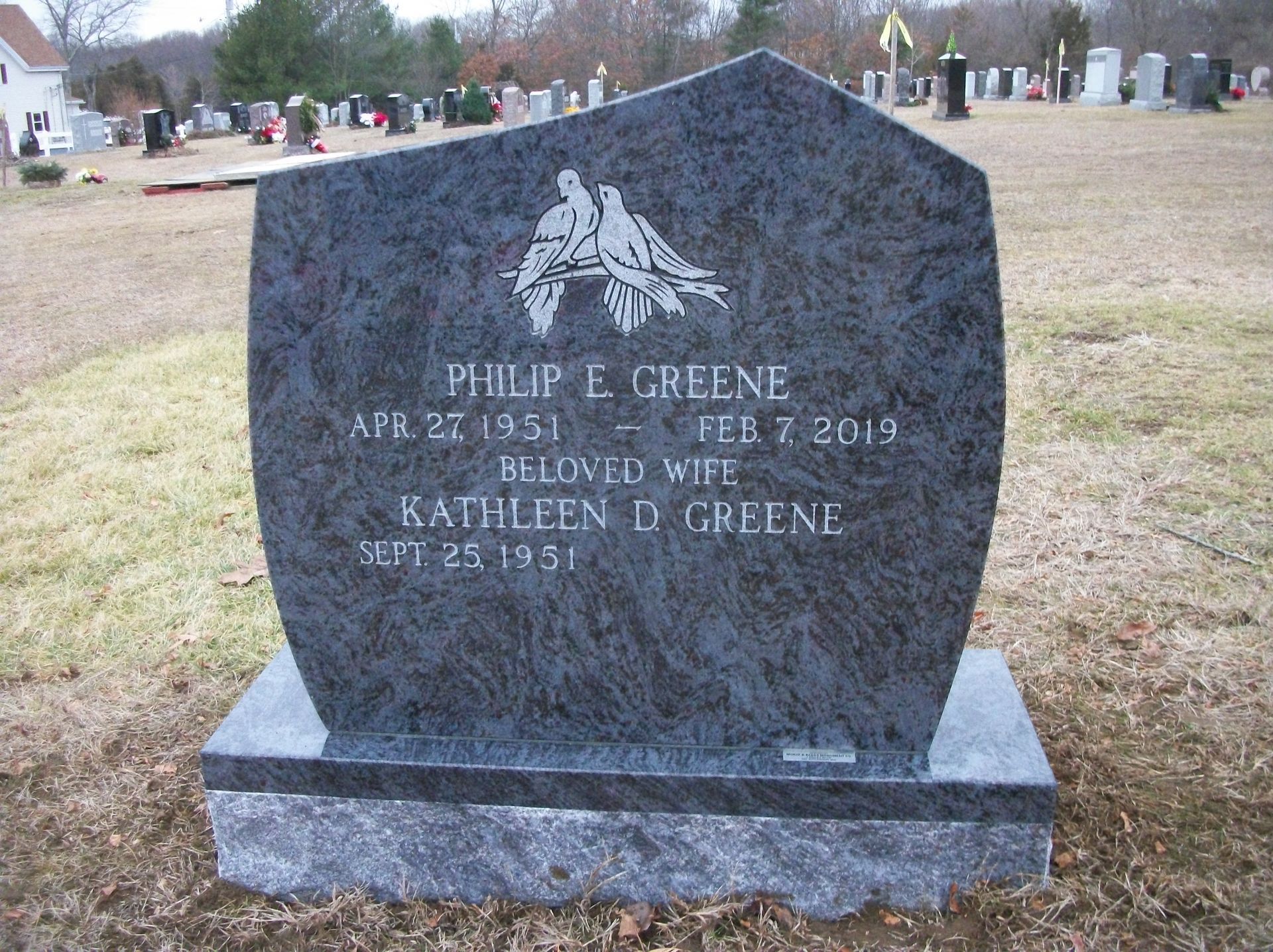 A polished dark granite gravestone in a cemetery with the names Philip E. Greene and Kathleen D. Greene etched on it.