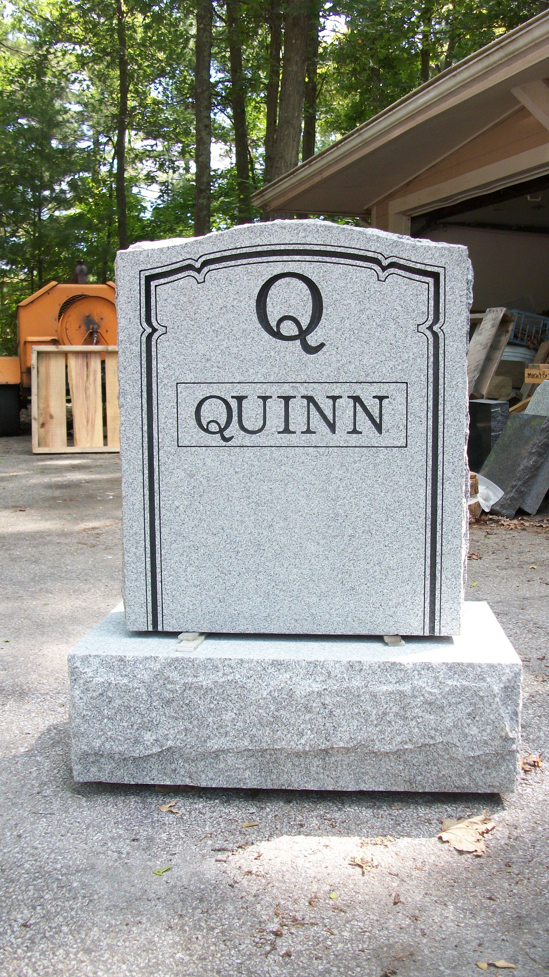A light grey granite headstone engraved with the letter 