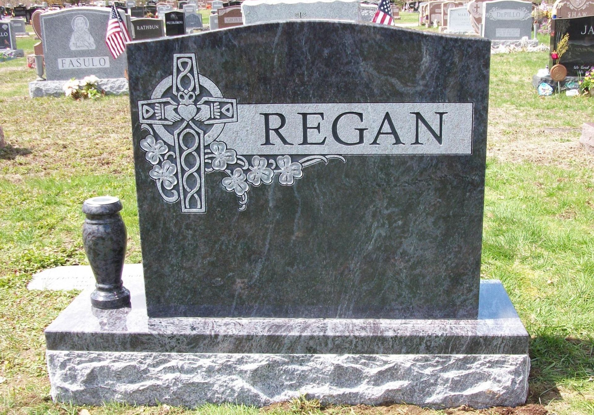 A dark granite headstone in a cemetery with a carved Celtic cross, the surname 