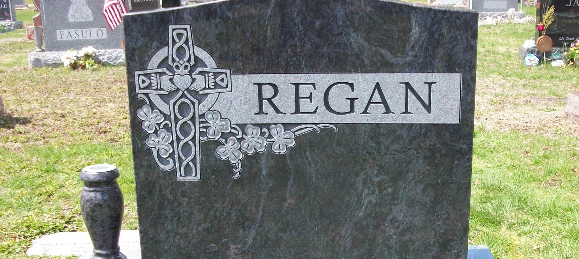 Headstones of various shapes and sizes stand in front of a building. Gray stone. Headstone Restoration Service Norton MA