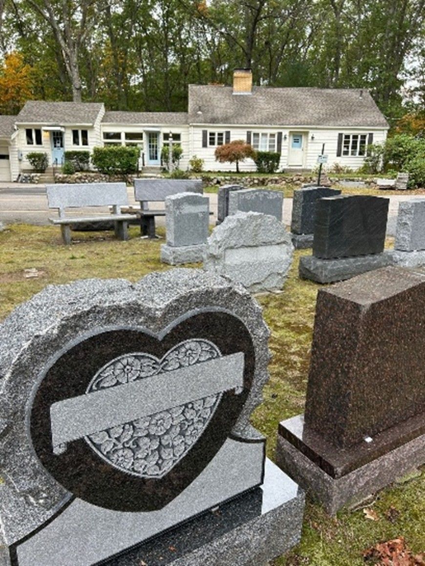 Granite monuments and headstones on display with a heart-shaped memorial and floral banner engraving
