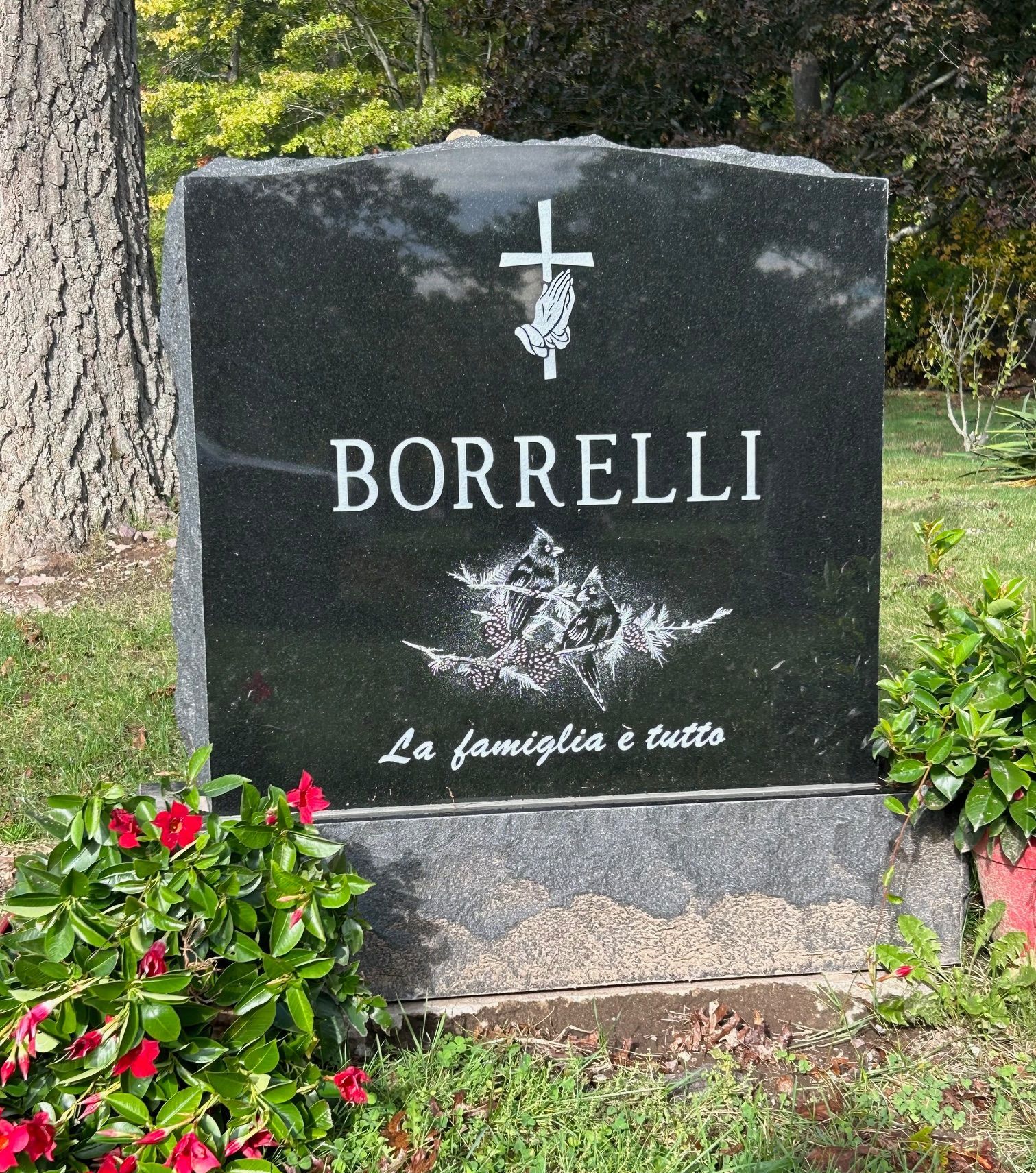 A black granite headstone with a cross, praying hands, etched cardinal birds, and the words 