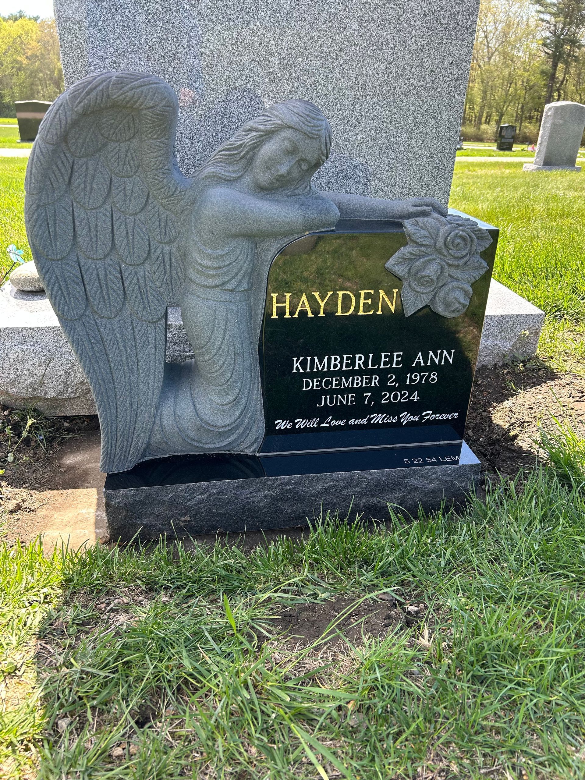 A gravestone featuring a gray stone angel leaning against a black plaque engraved with the name Hayden and dates.
