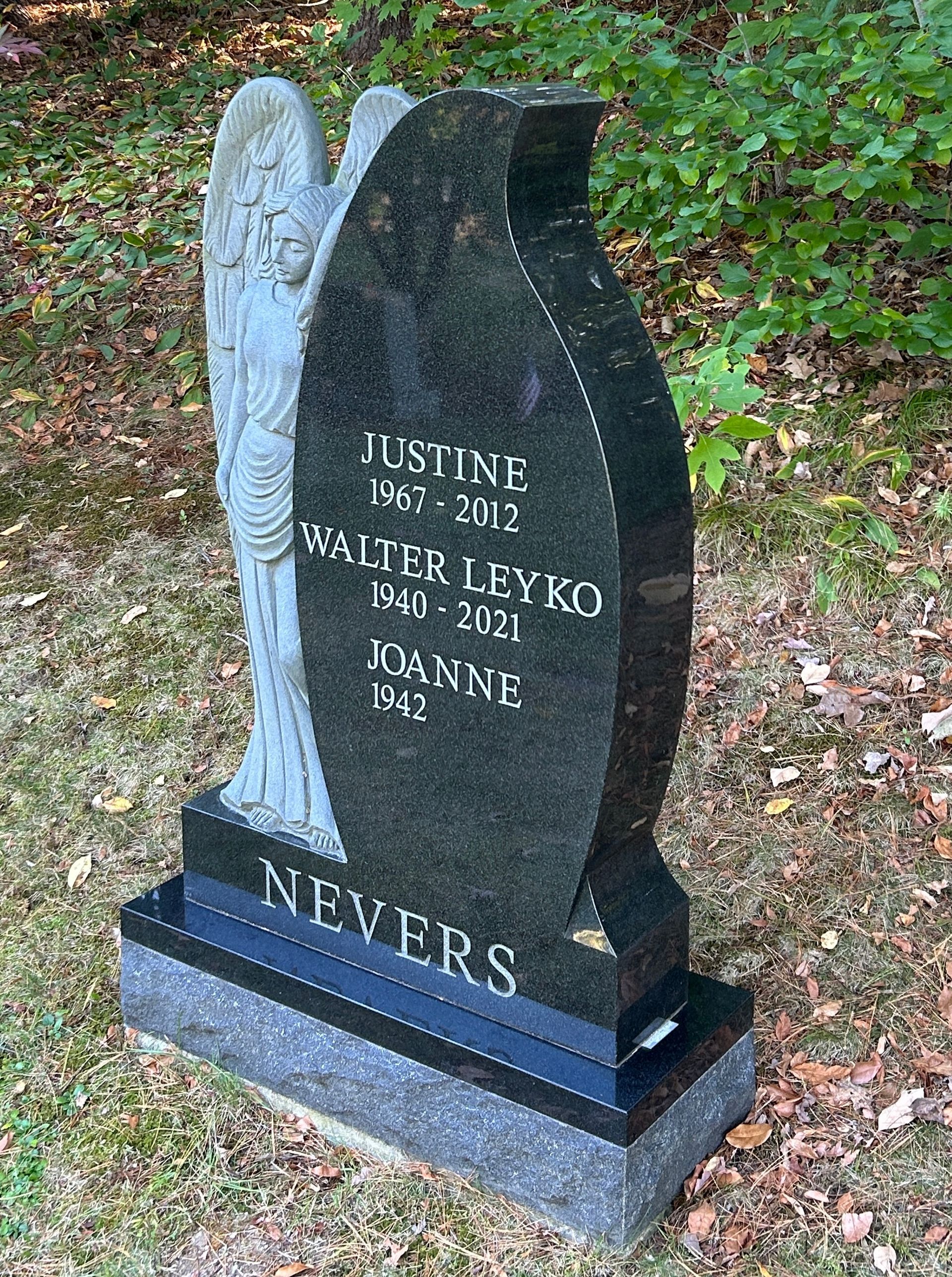 A black, teardrop-shaped granite headstone with a carved angel on the side, inscribed with the name NEVERS.