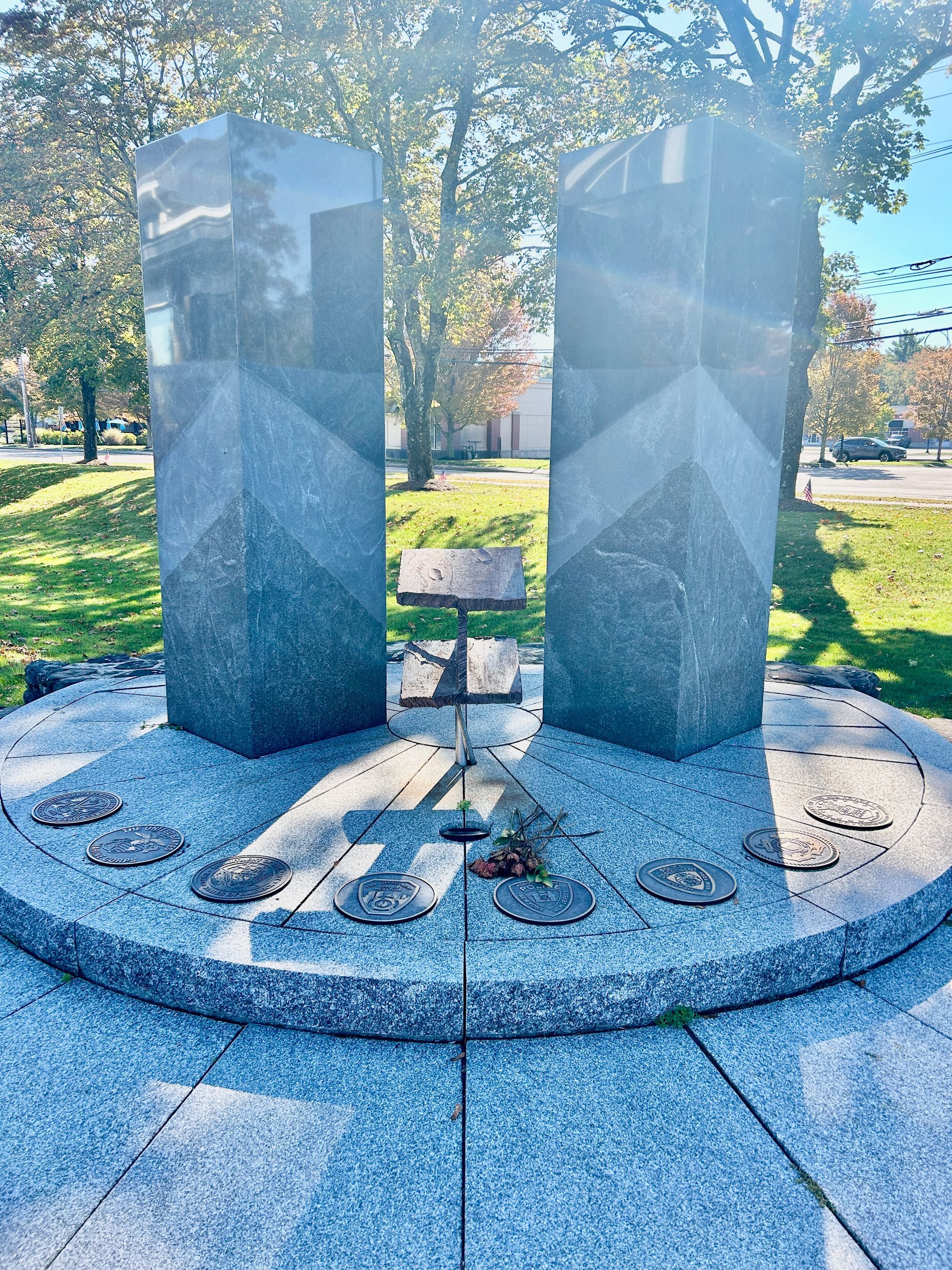 A granite monument featuring two tall pillars and a central pedestal, set on a circular stone base in a park.
