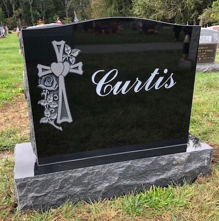 A black granite upright headstone with a cross, heart, and floral engraving, inscribed with 