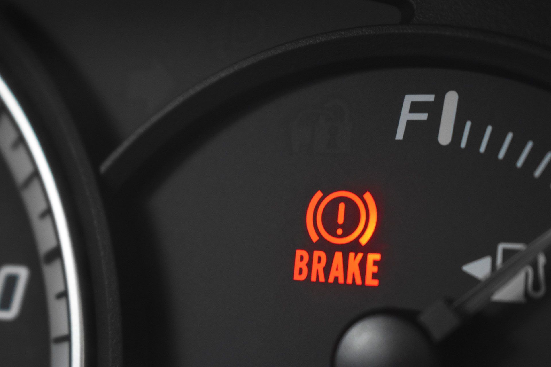 Red illuminated brake warning light on a car dashboard.