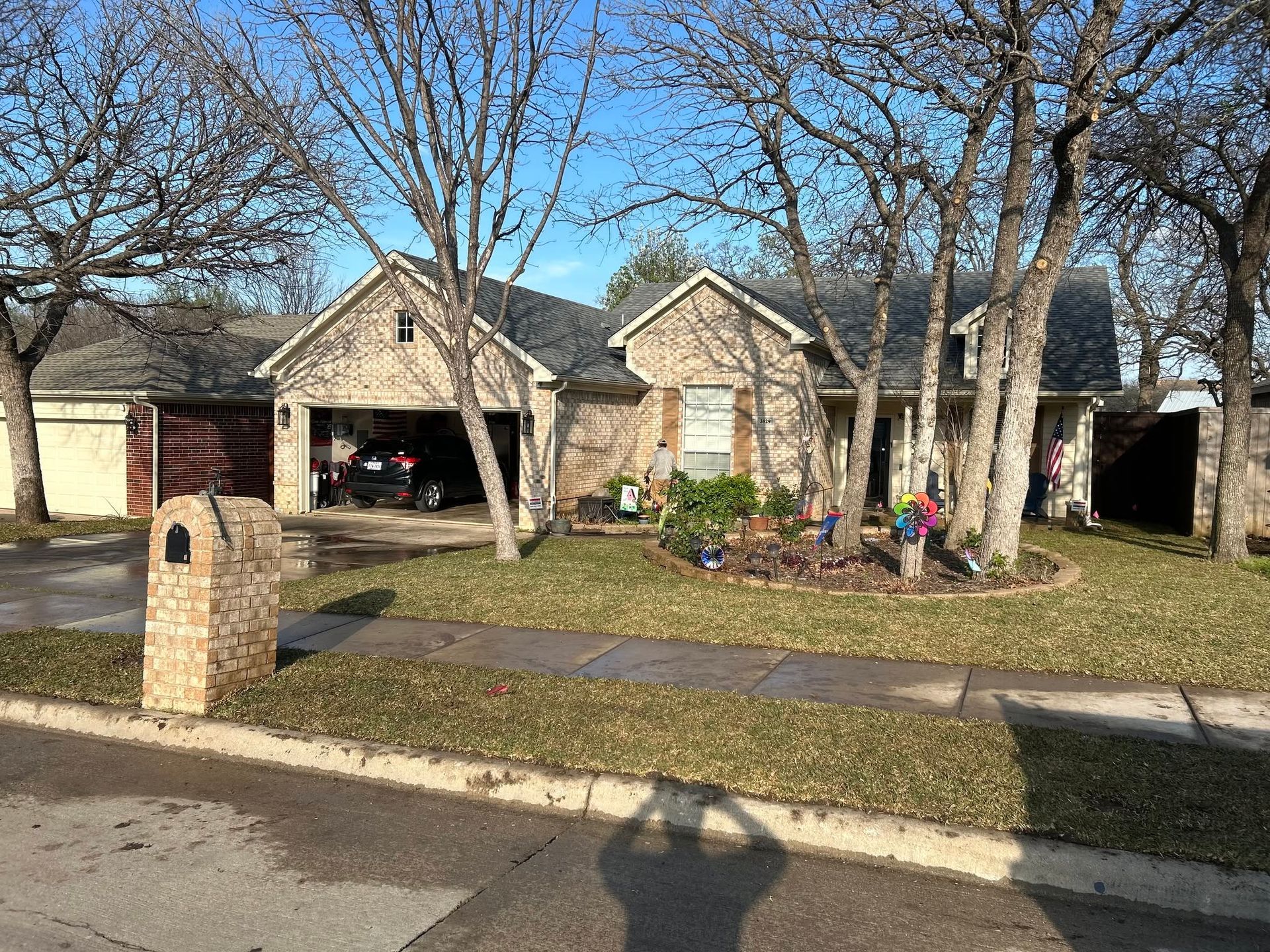 Suburban house with stone facade, open garage, leafless trees, and a front yard in daylight