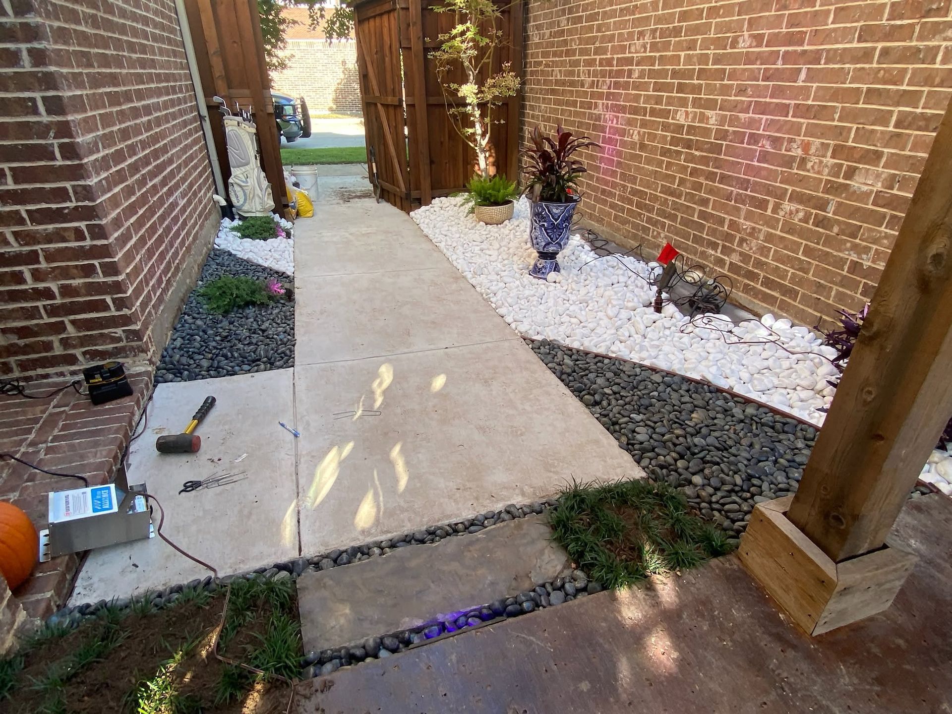 Narrow concrete walkway between brick walls, with white gravel borders and small garden lights.