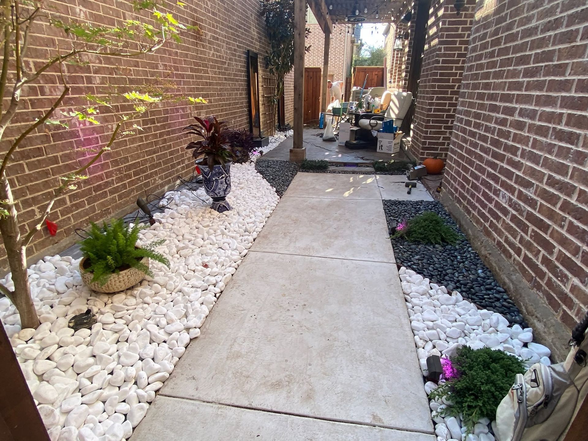 Narrow brick alley with concrete walkway and white gravel garden borders, leading to bins in the distance