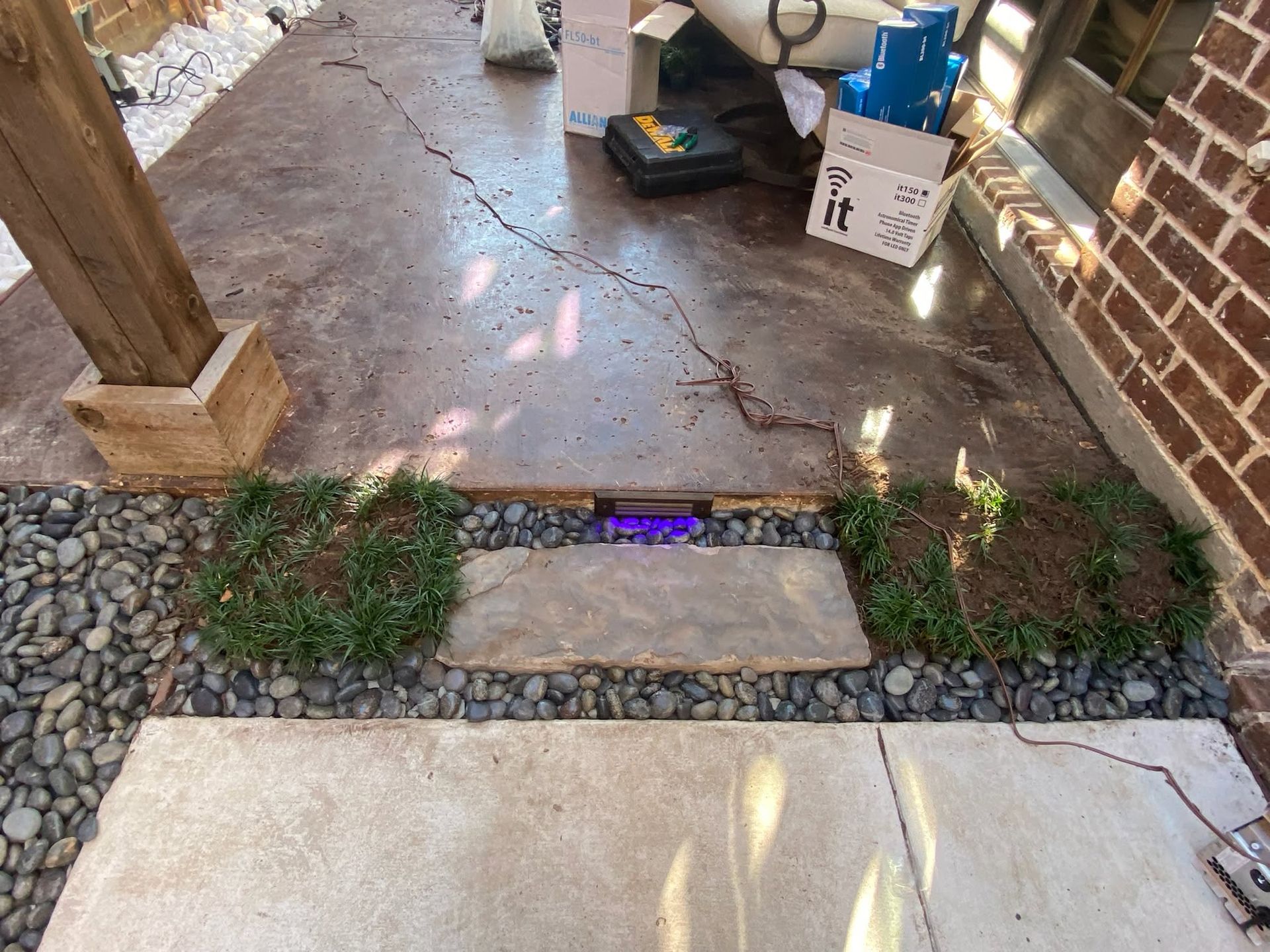 Brick porch with small stone path, potted plants, and a cardboard box near the doorway