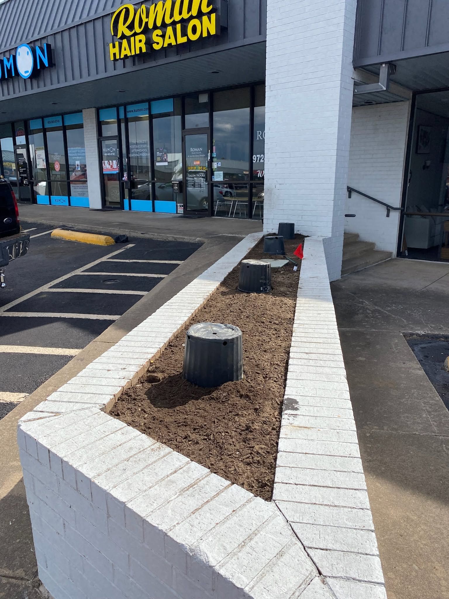 Outdoor strip mall planter with white brick walls, brown mulch, and a storefront in the background