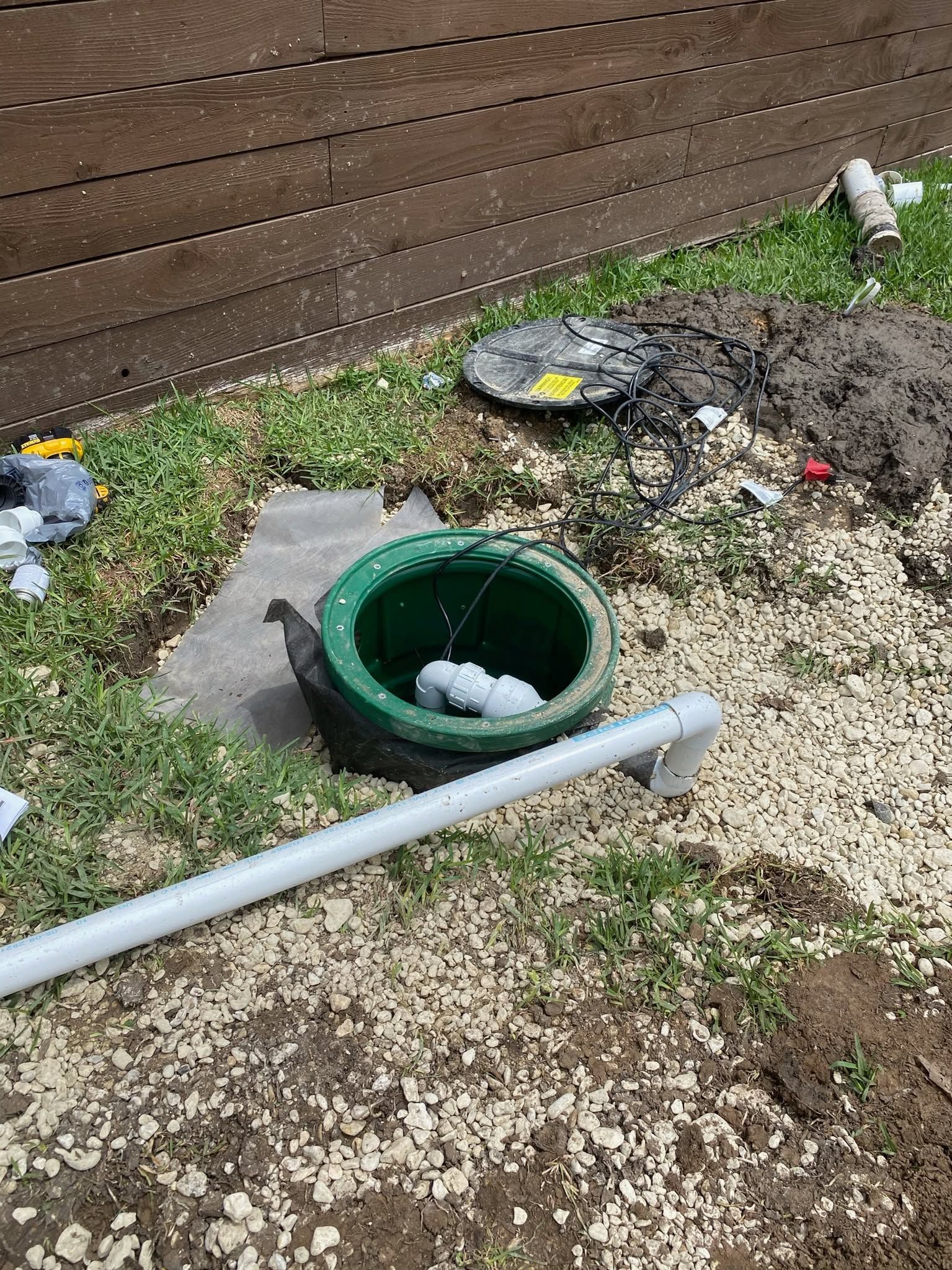Backyard with a green tire planter, muddy ground, and a gray pipe near a wooden fence