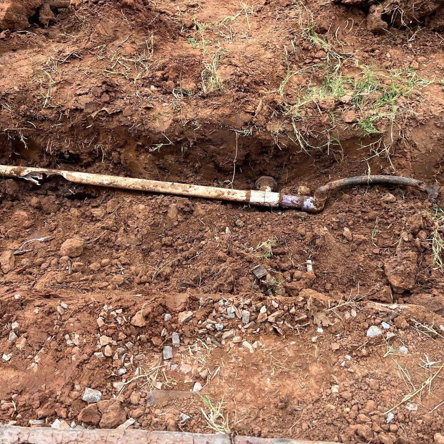 A dirt trench exposing a long pipe with a joint and attached black hose.