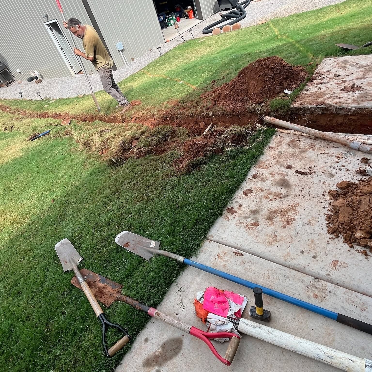 Tree uprooted across sidewalk and lawn; worker in background, shovels and yard tools in foreground.