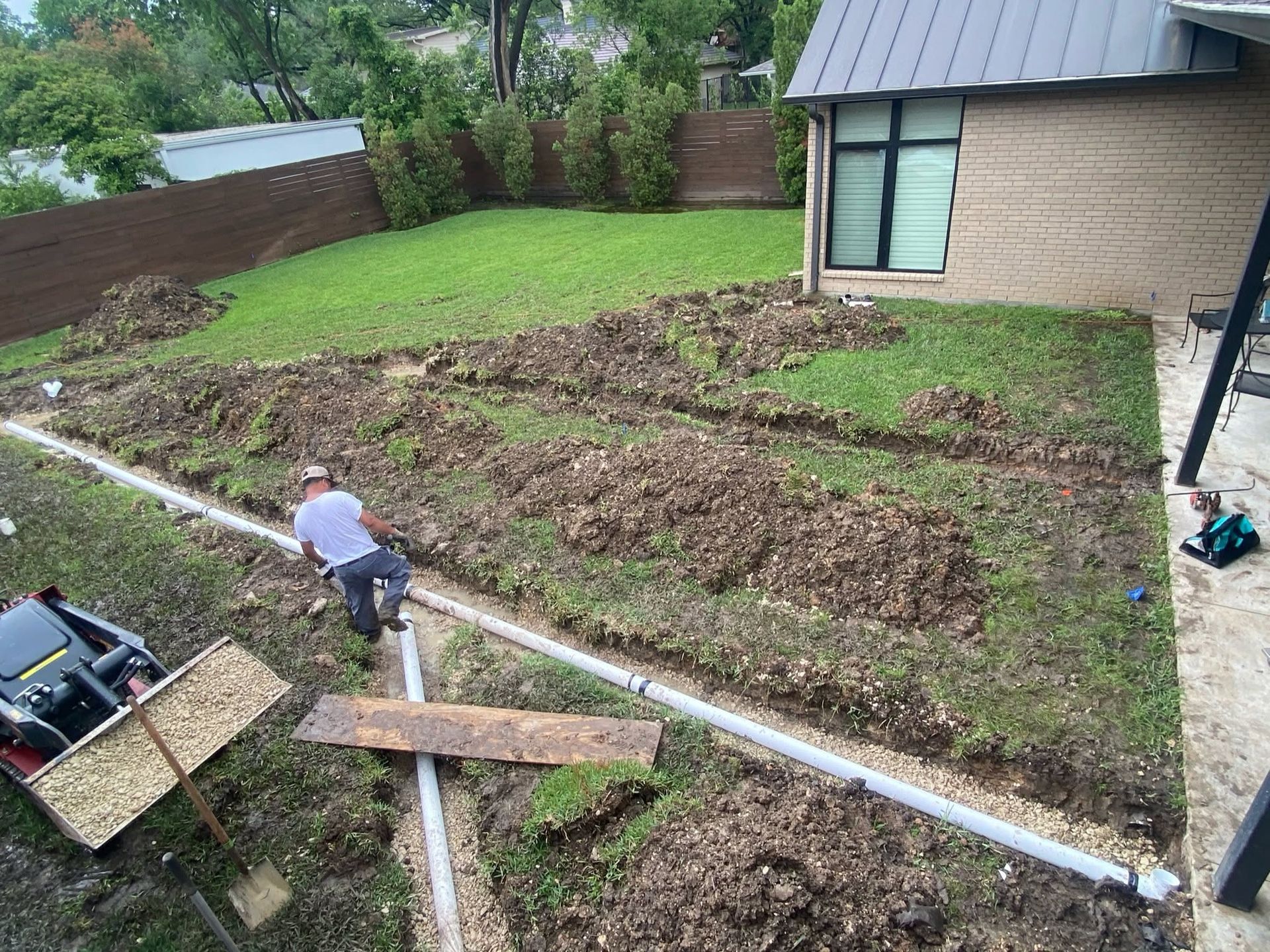 Person spreading mulch in a backyard garden beside a house and raised beds