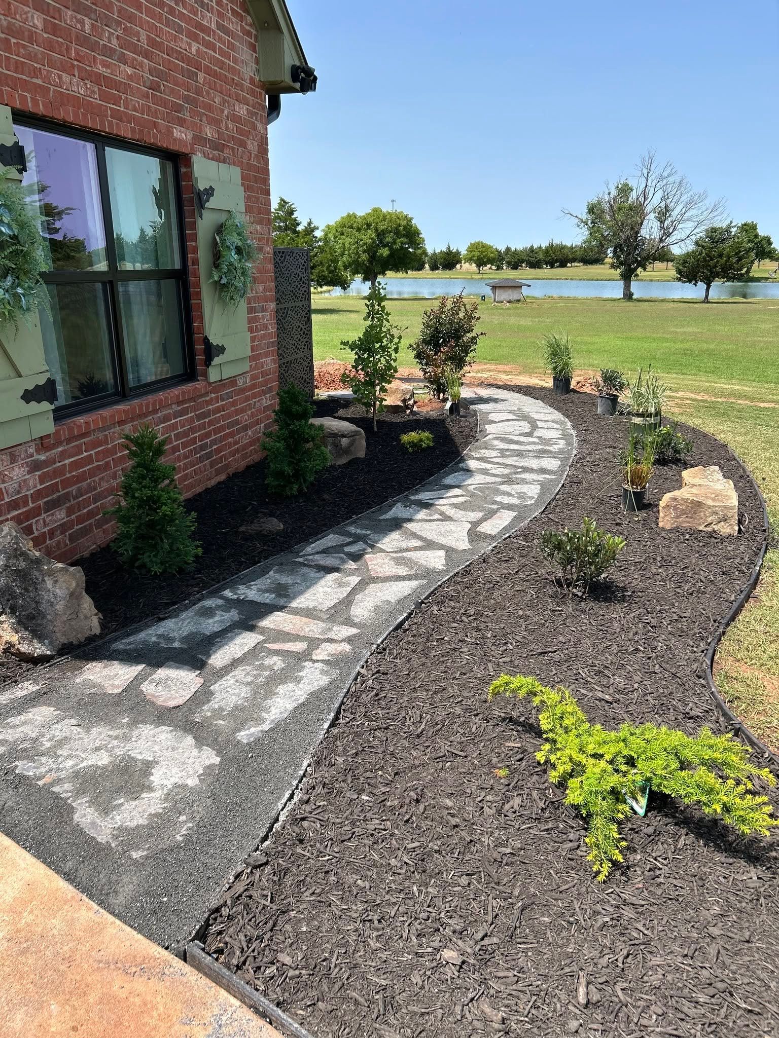 Brick house with curved stone path beside a mulched garden and green lawn by the water.