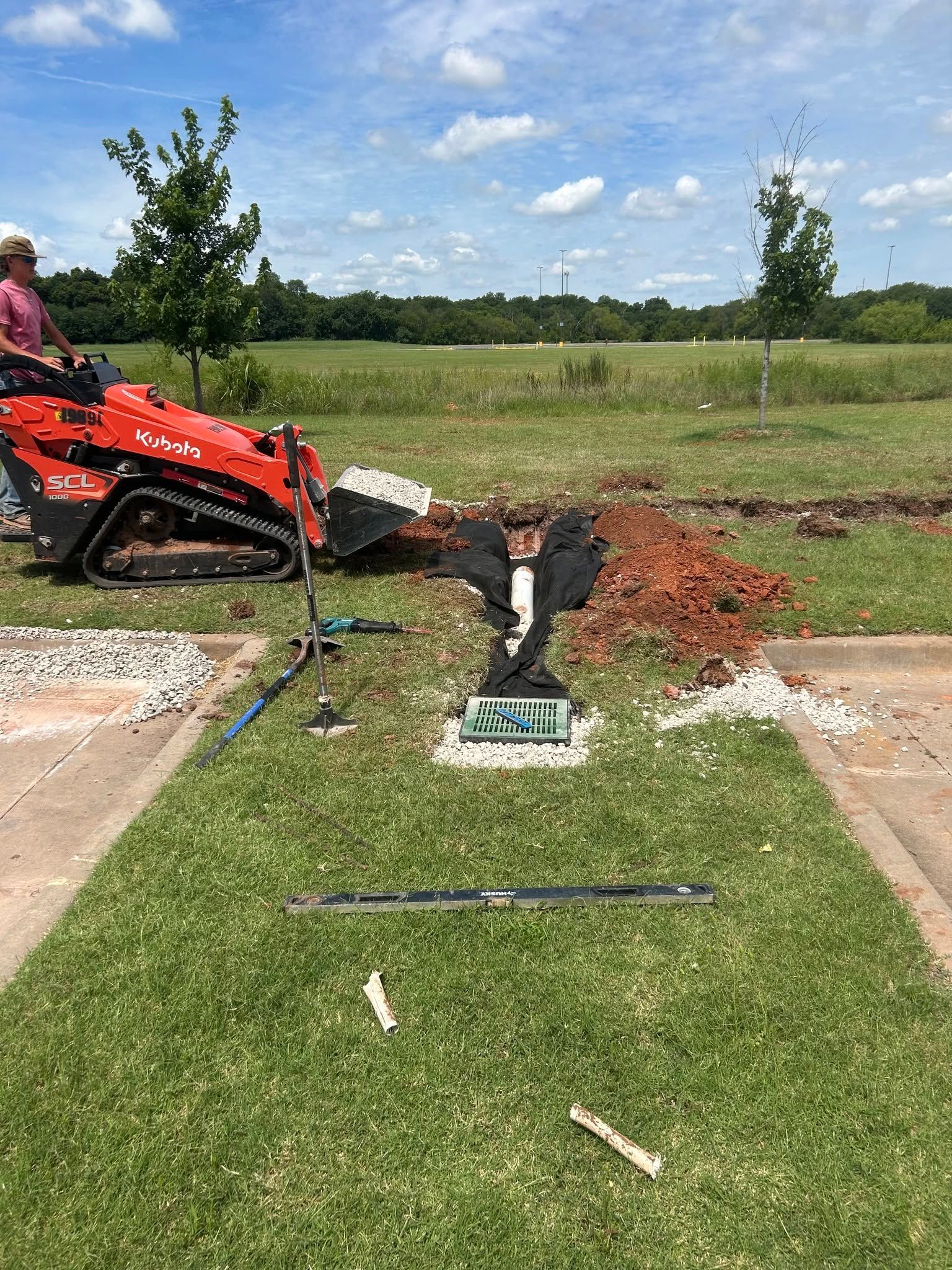 Red lawn mower cutting a green field with a trench and exposed dirt under a blue sky.