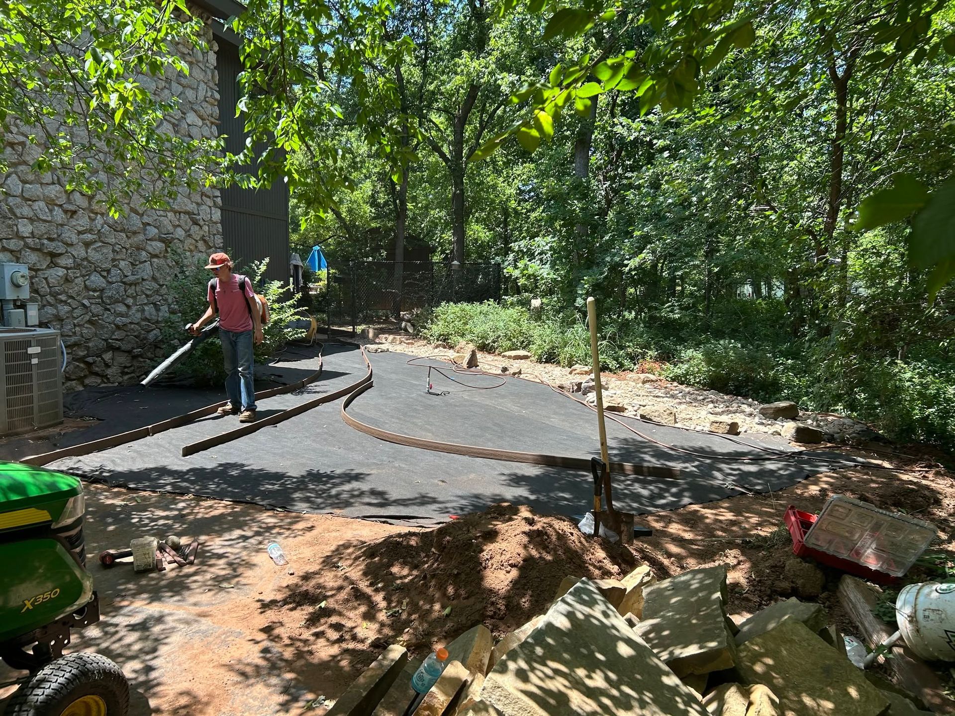 Person in red shirt smoothing wet pavement in a wooded outdoor area