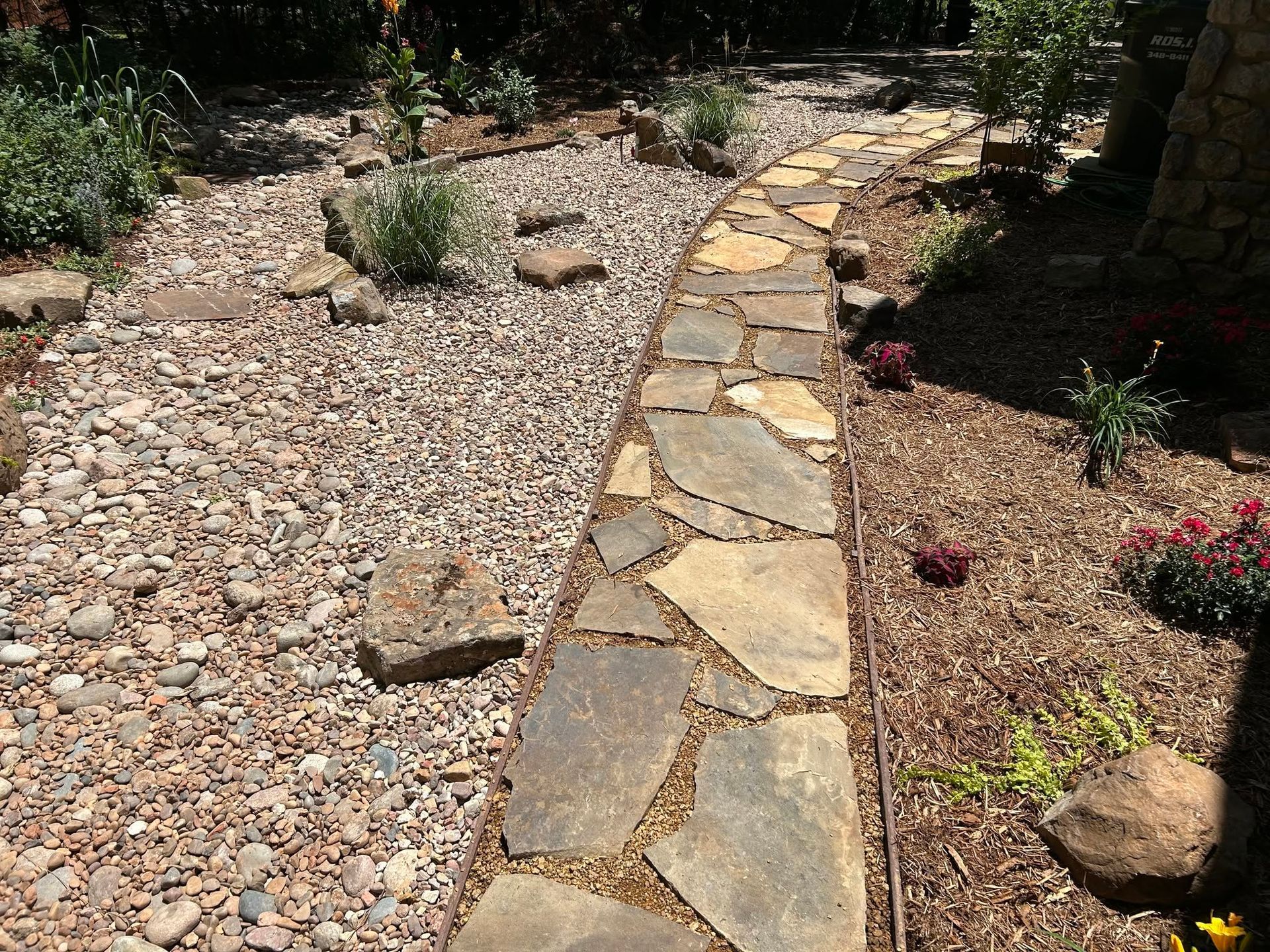 Stone garden path winding through gravel and flower beds in a sunlit yard