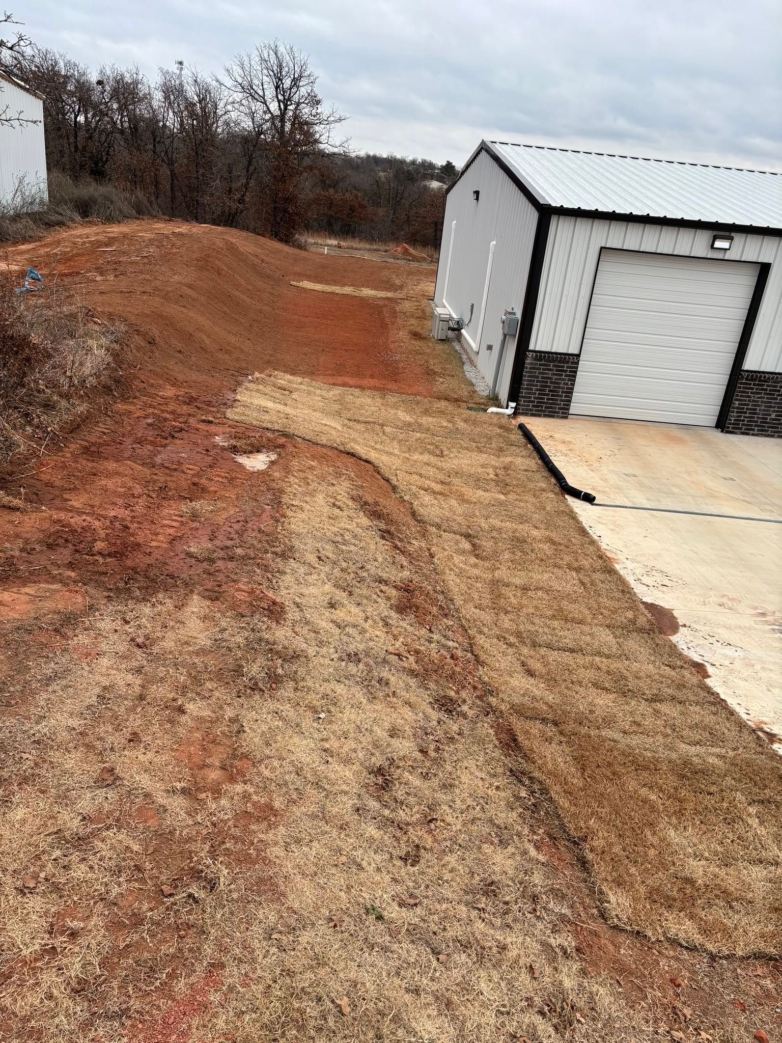 Gravel driveway beside a white garage, with a dirt slope and brush in the background.