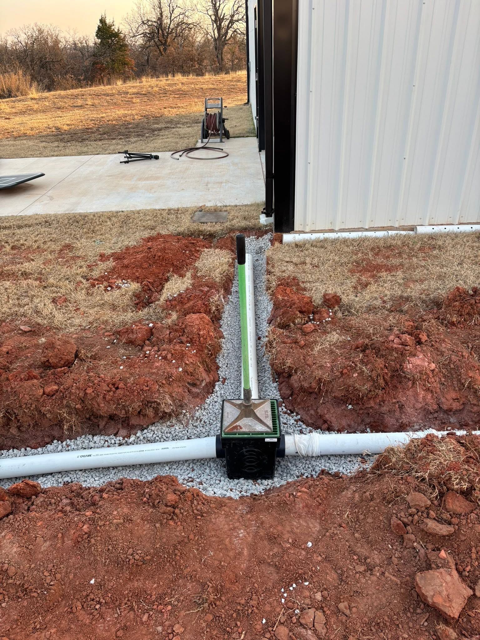 Roof drain pipe between two metal buildings over gravel and dirt, with a small support post in the foreground