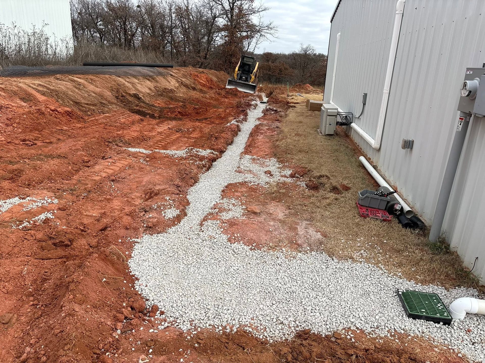 Gravel path through red dirt beside a white building, with construction equipment in the distance.