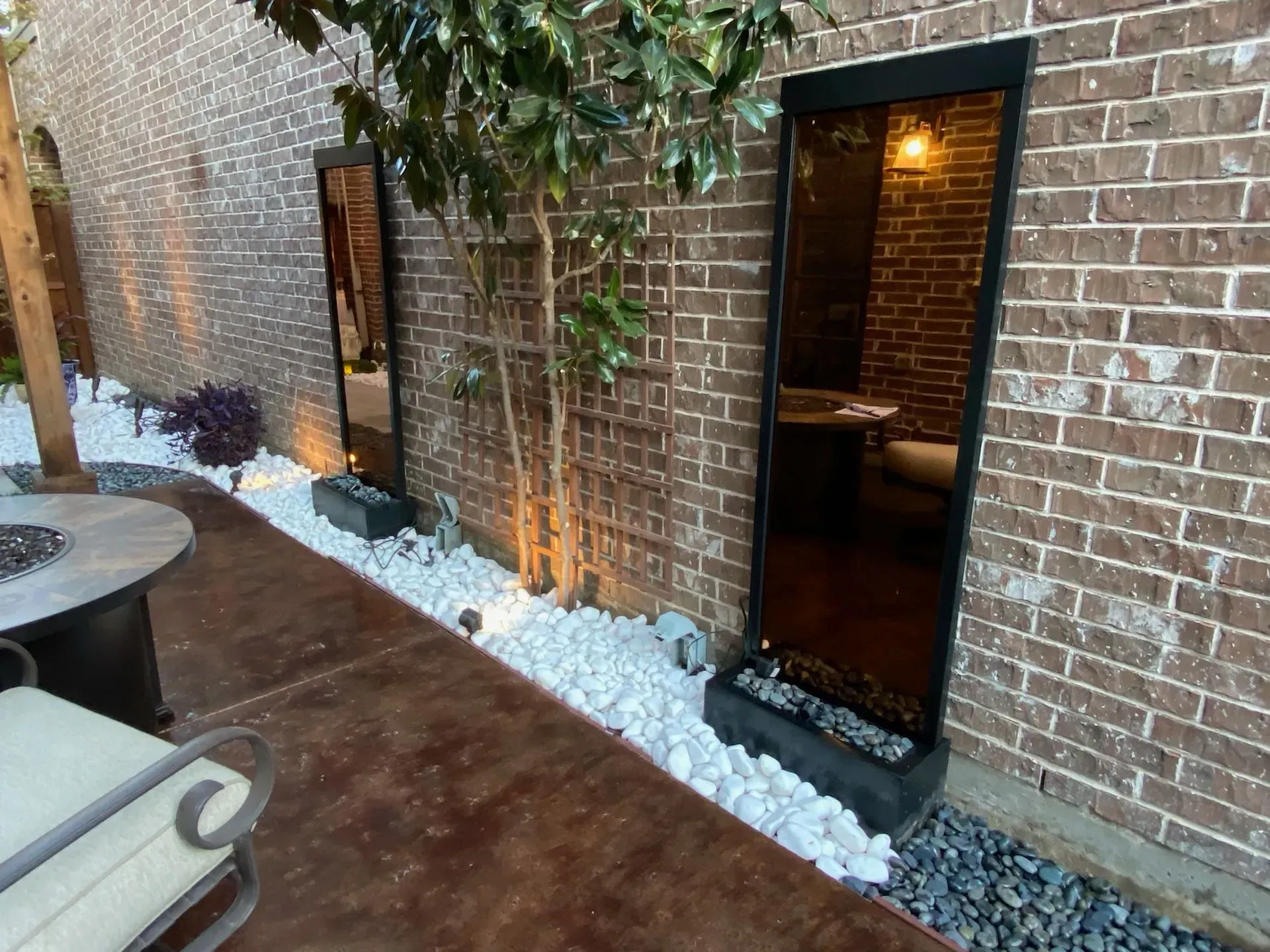 Brick patio with a lit doorway, vine-covered wall, and white decorative stones along the edge