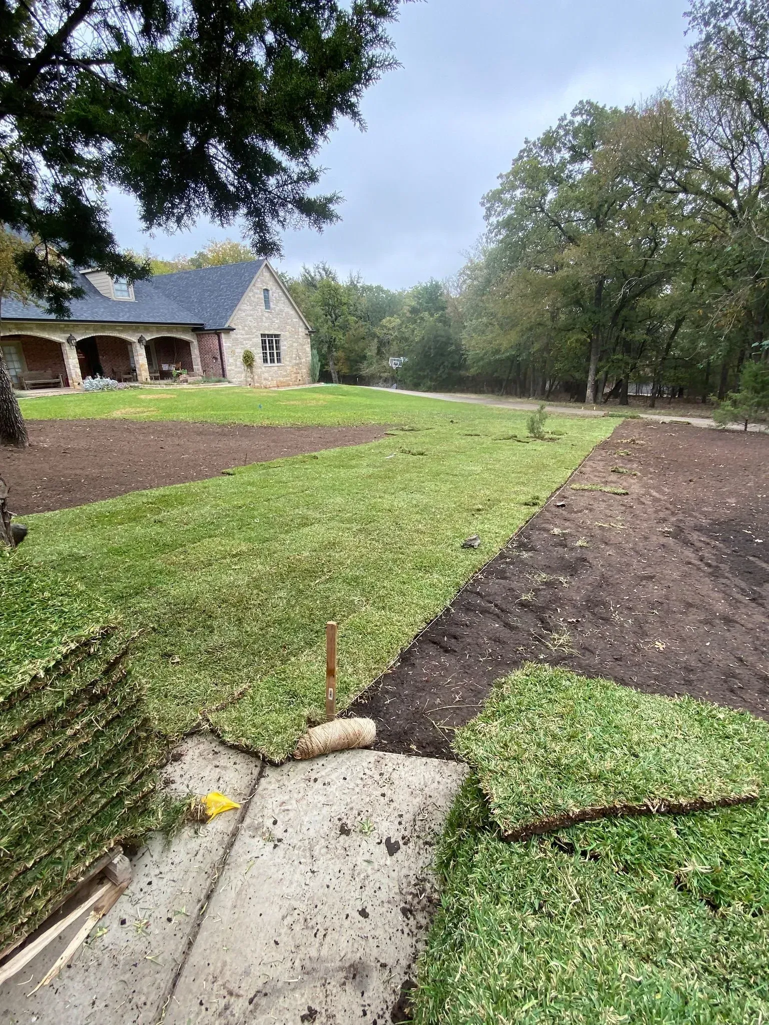 Stone house beside freshly landscaped lawn and dark mulch beds under a cloudy sky.
