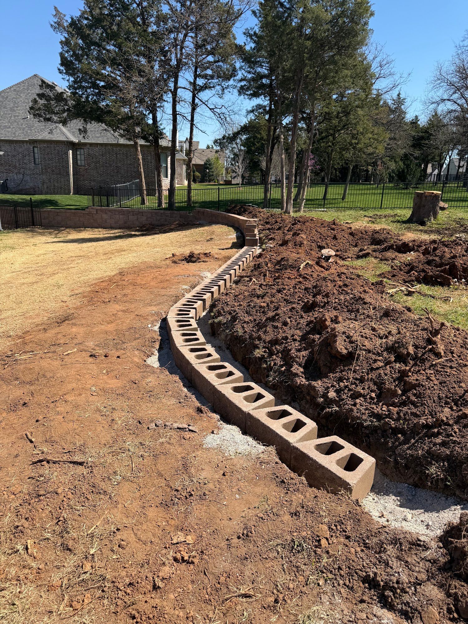 Curved cinder block border beside a dirt path and fresh landscaping in a sunny yard