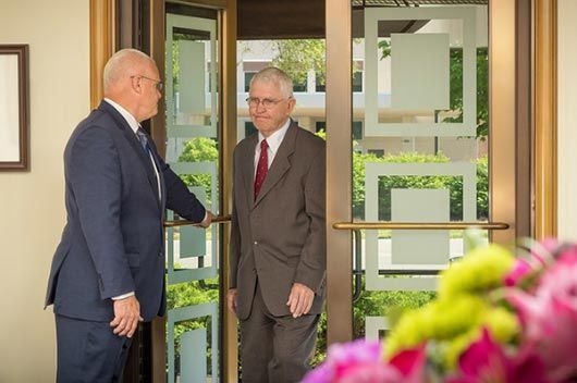 two men in suits are shaking hands in front of a door .