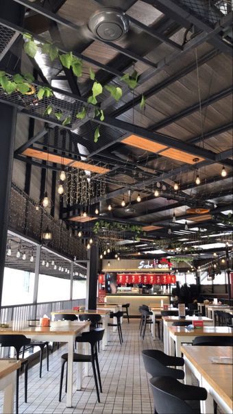 Interior de restaurante moderno com teto alto preto, plantas suspensas e fileiras de mesas e cadeiras.