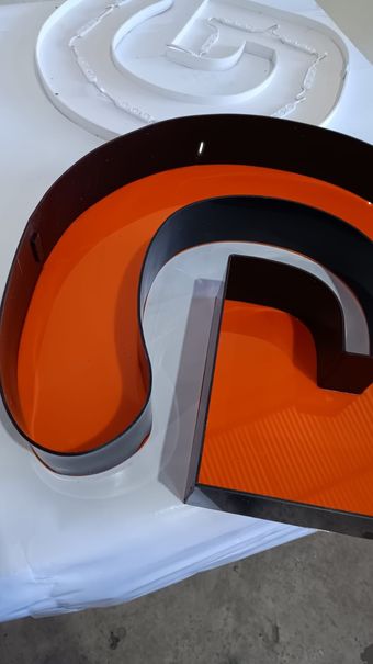 Letras do logotipo em laranja, preto e branco sobre fundo branco.