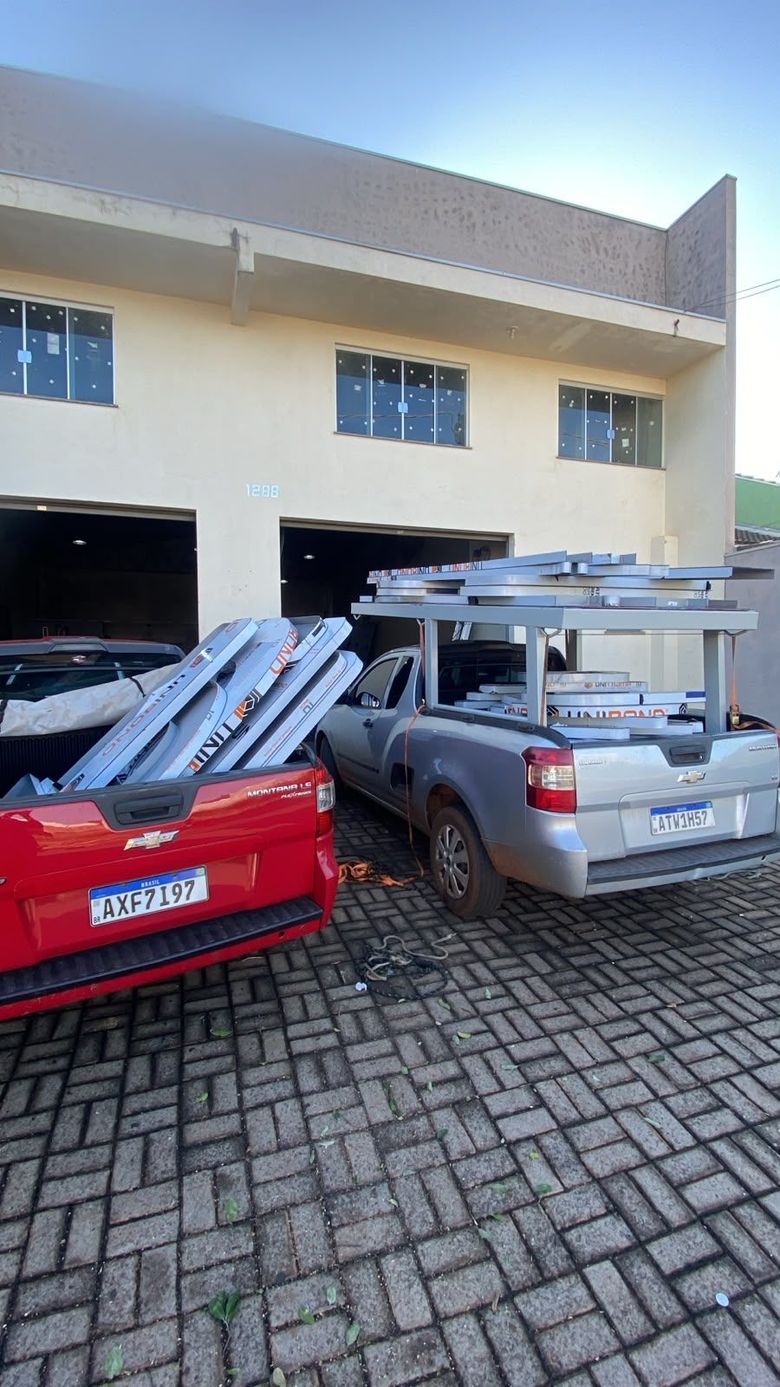 Dois carros estacionados em frente a um prédio, carregados com canos de metal e bagageiros de teto.