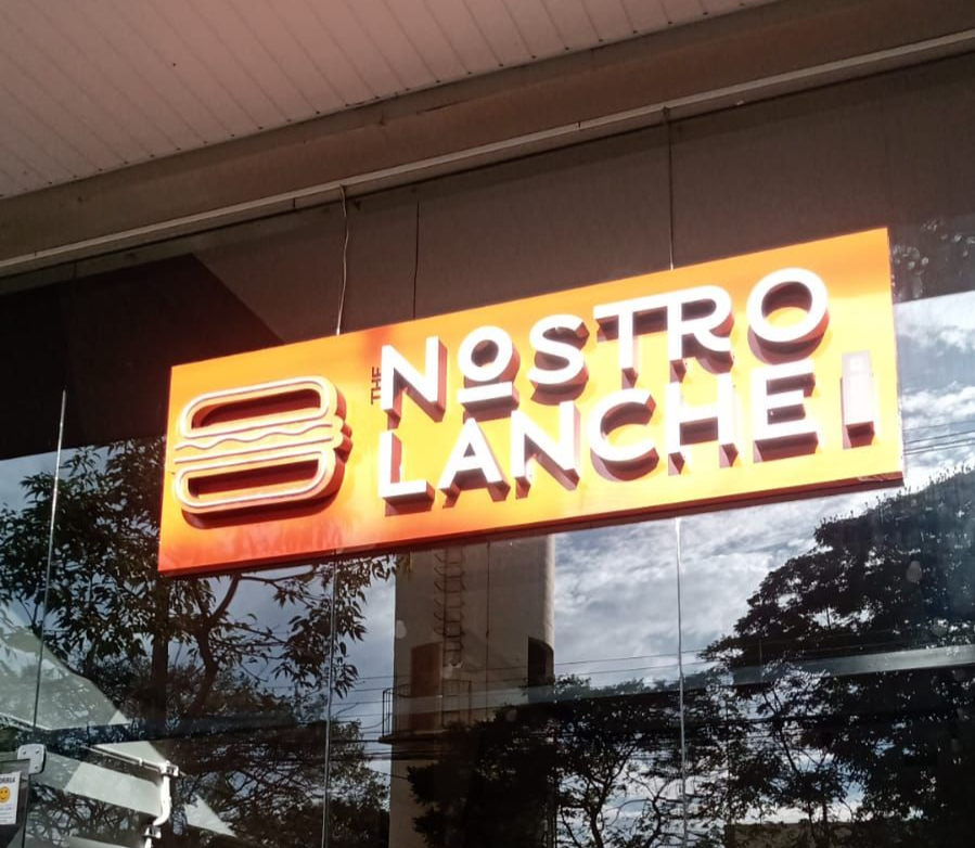 Letreiro laranja iluminado com a inscrição “Bistro Blanche” em uma fachada de vidro sob uma cobertura.