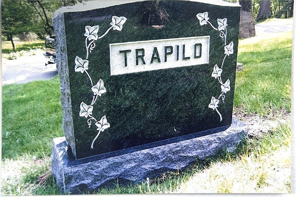 Black gravestone monument with a carved angel wing on a stone base outdoors in a cemetery.
