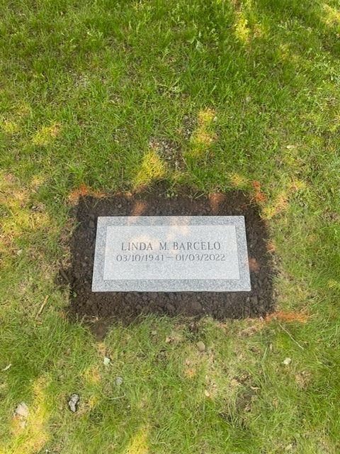 Rectangular memorial plaque set in grass, bordered by dark mulch and small yellow flowers.