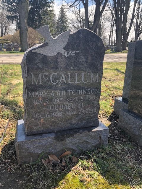 McCallum gravestone with dove engraving in a cemetery, shown among trees and grass