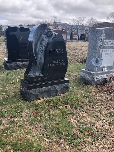 Gravestone for Gerald Fusco in a cemetery, with a winged angel sculpture and snowy background.