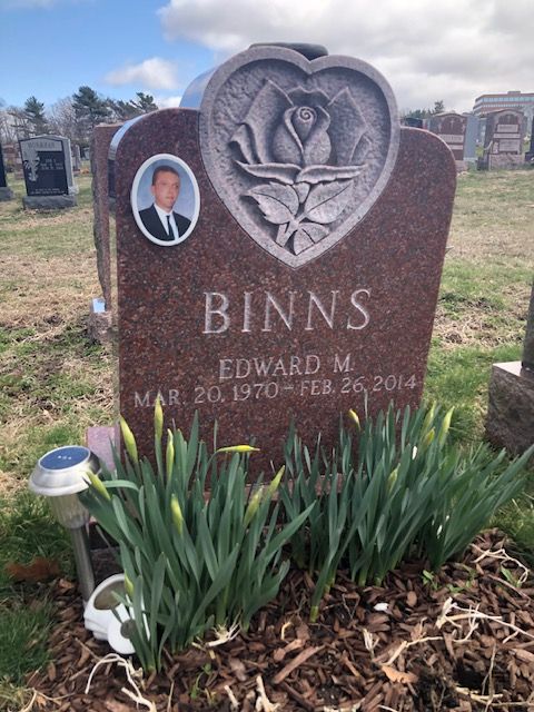 Binns gravestone with heart-shaped angel carving and an oval photo portrait, surrounded by flowers