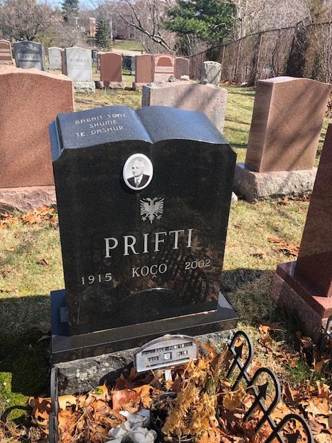 Black granite memorial headstone in a cemetery with carved open book and surrounding graves.