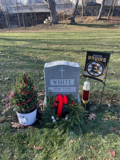 Gravestone memorial with flowers, wreath, and candle in a grassy cemetery area