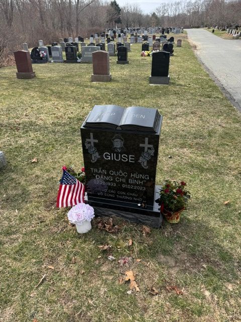 Gravestone with American flag, flowers, and a white lantern in a cemetery