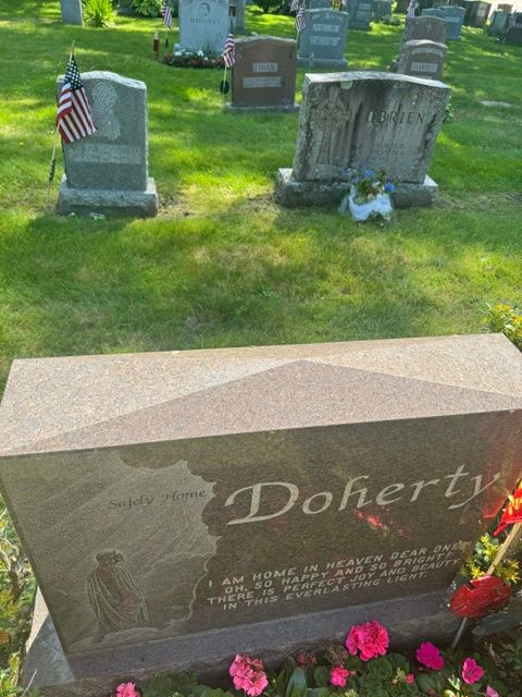 Doherty gravestone with pink flowers in a cemetery, with other headstones in the background