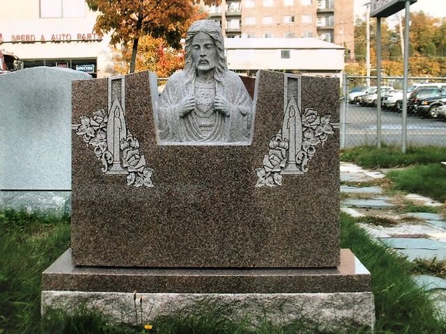 Stone memorial with a carved bust and decorative panels in an outdoor plaza.