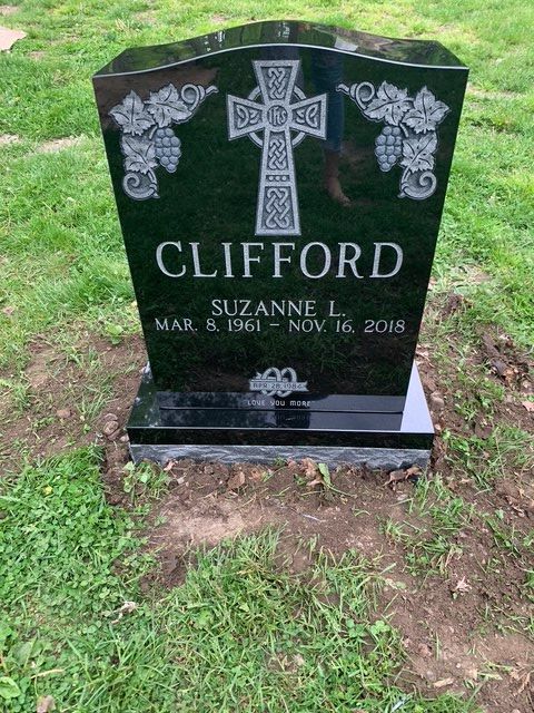 Black granite gravestone for Clifford Suzanne with Celtic cross and floral engravings in a grassy cemetery.