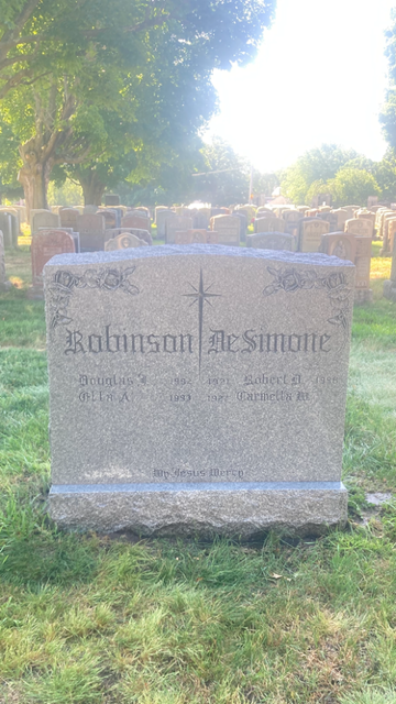 Sunlit gravestone in a cemetery, surrounded by grass and trees.